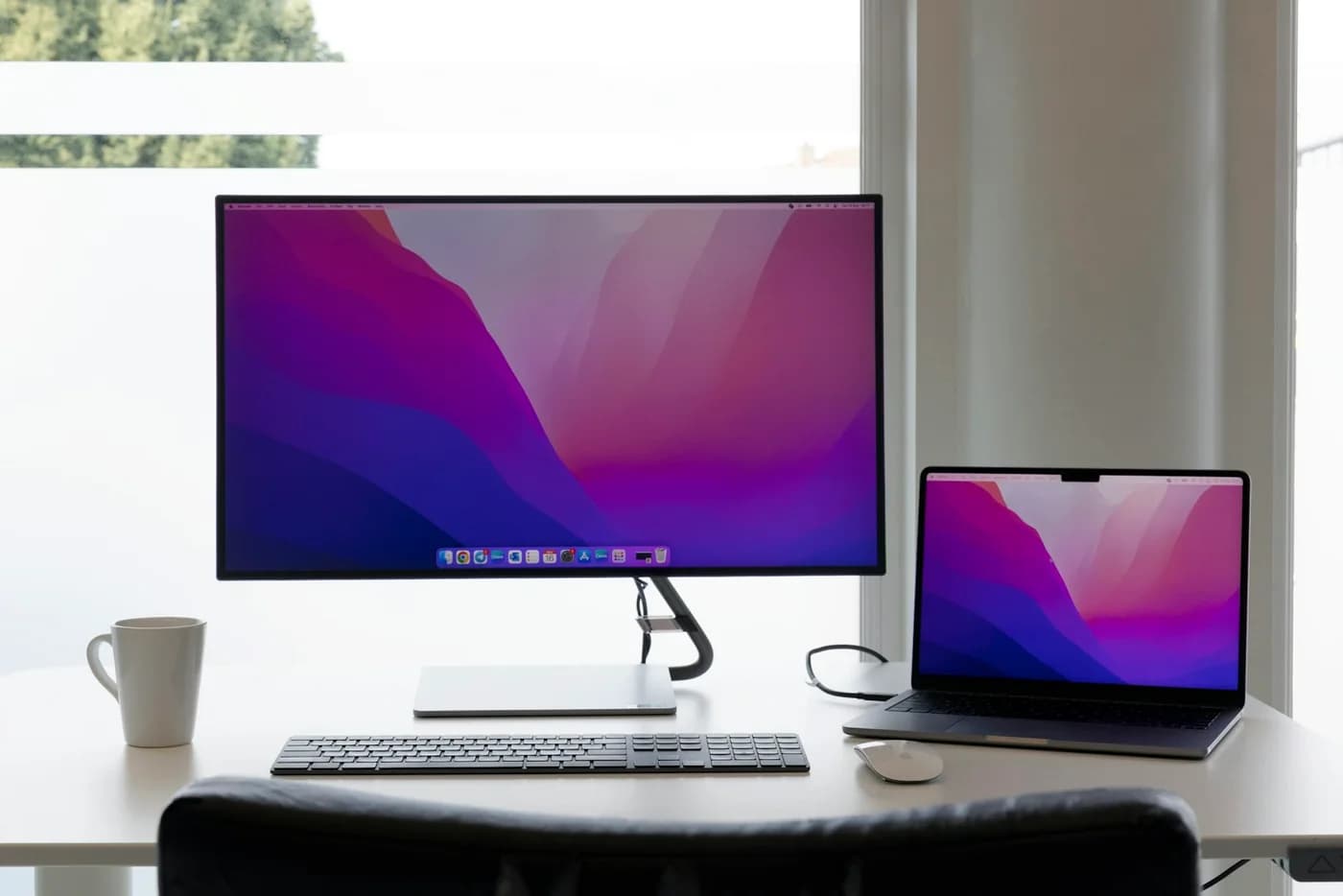 Desktop display and laptop with violet screens in a minimal workspace